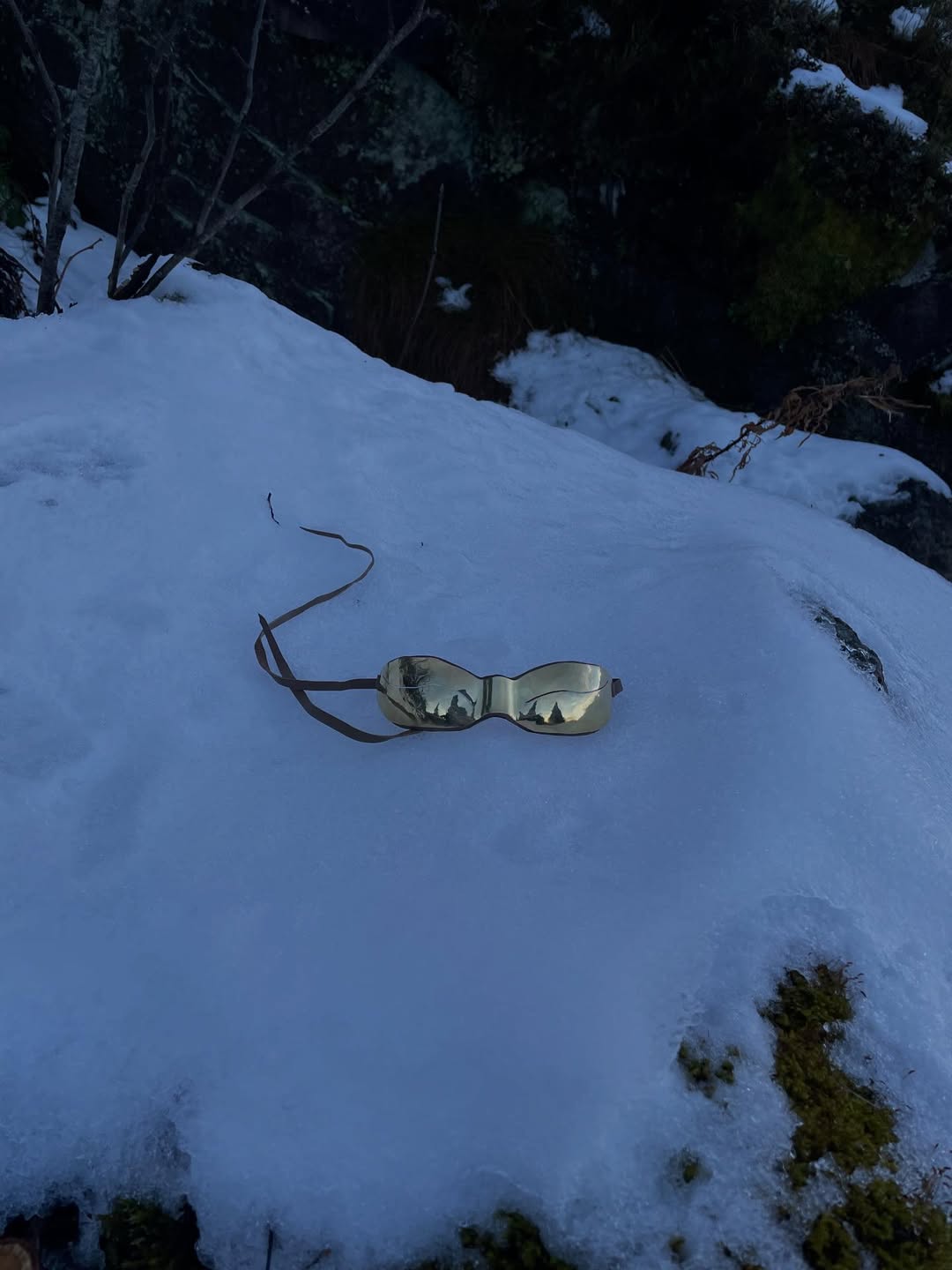 Brass cat-shape snow goggles resting on icy snow at dusk
