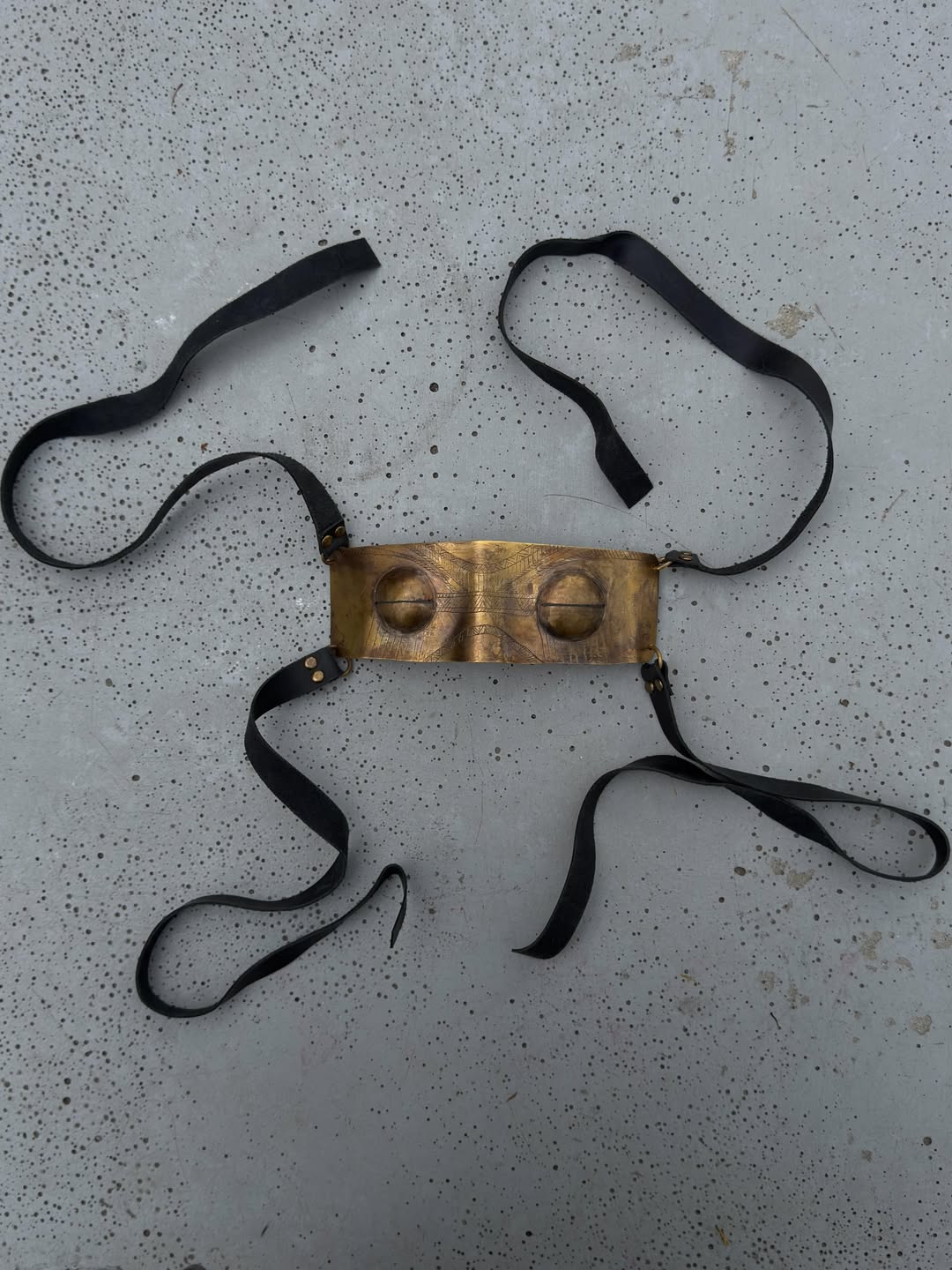 Brass Mask laid flat — hand-carved brass with patina finish and trailing leather straps