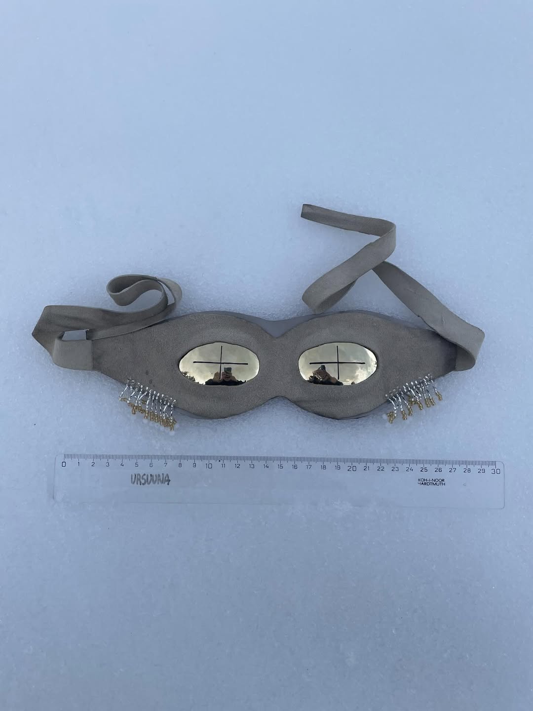 Brass beige suede snow goggles laid flat on snow with ruler and URSUUNA mark