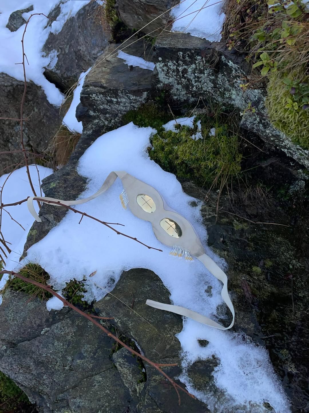 Brass beige suede snow goggles resting on snow and moss-covered Arctic rocks