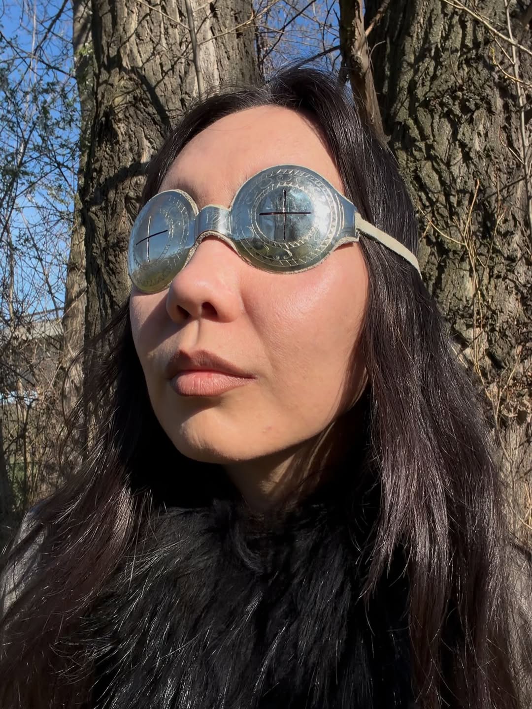 Oversized silver circle-shape Arctic goggles worn, with cross slits and beige leather lining