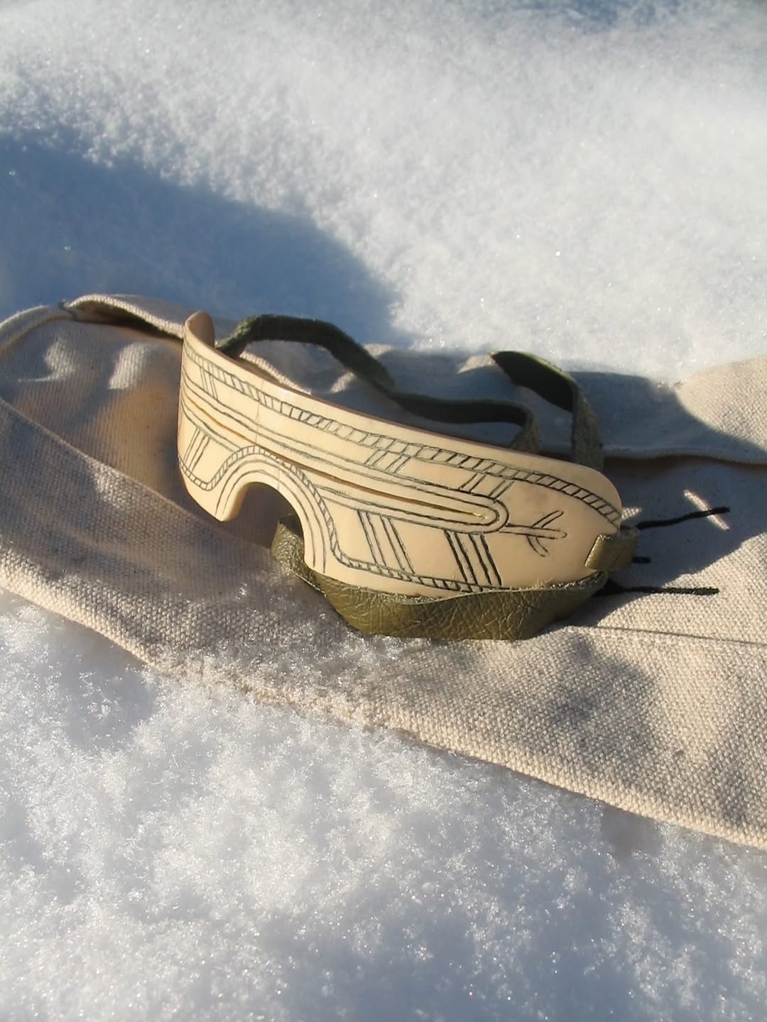 Mammoth ivory shield goggles side view showing carved ornamentation and teal leather strap