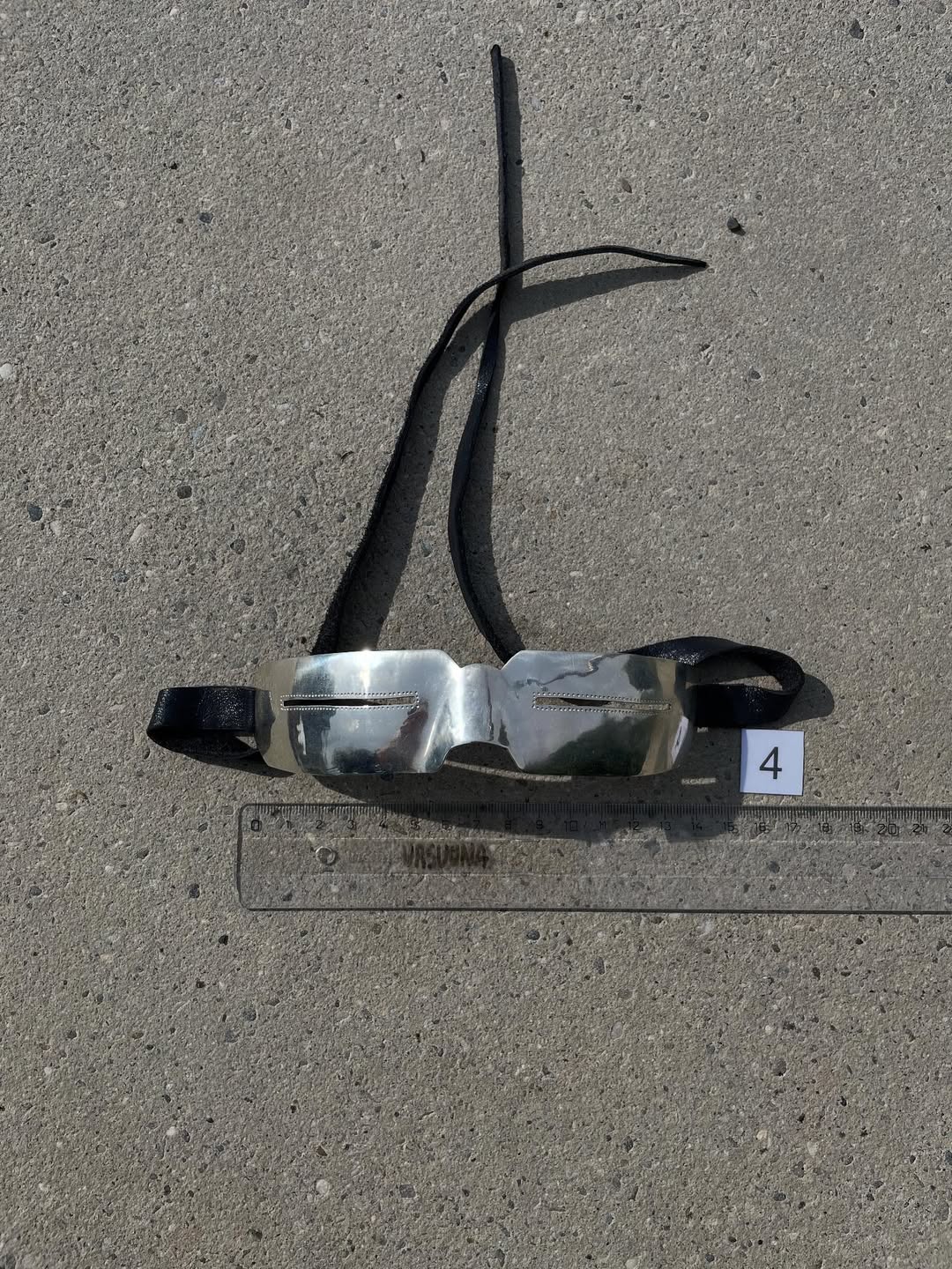 Silver goggles with dark blue leather straps laid out