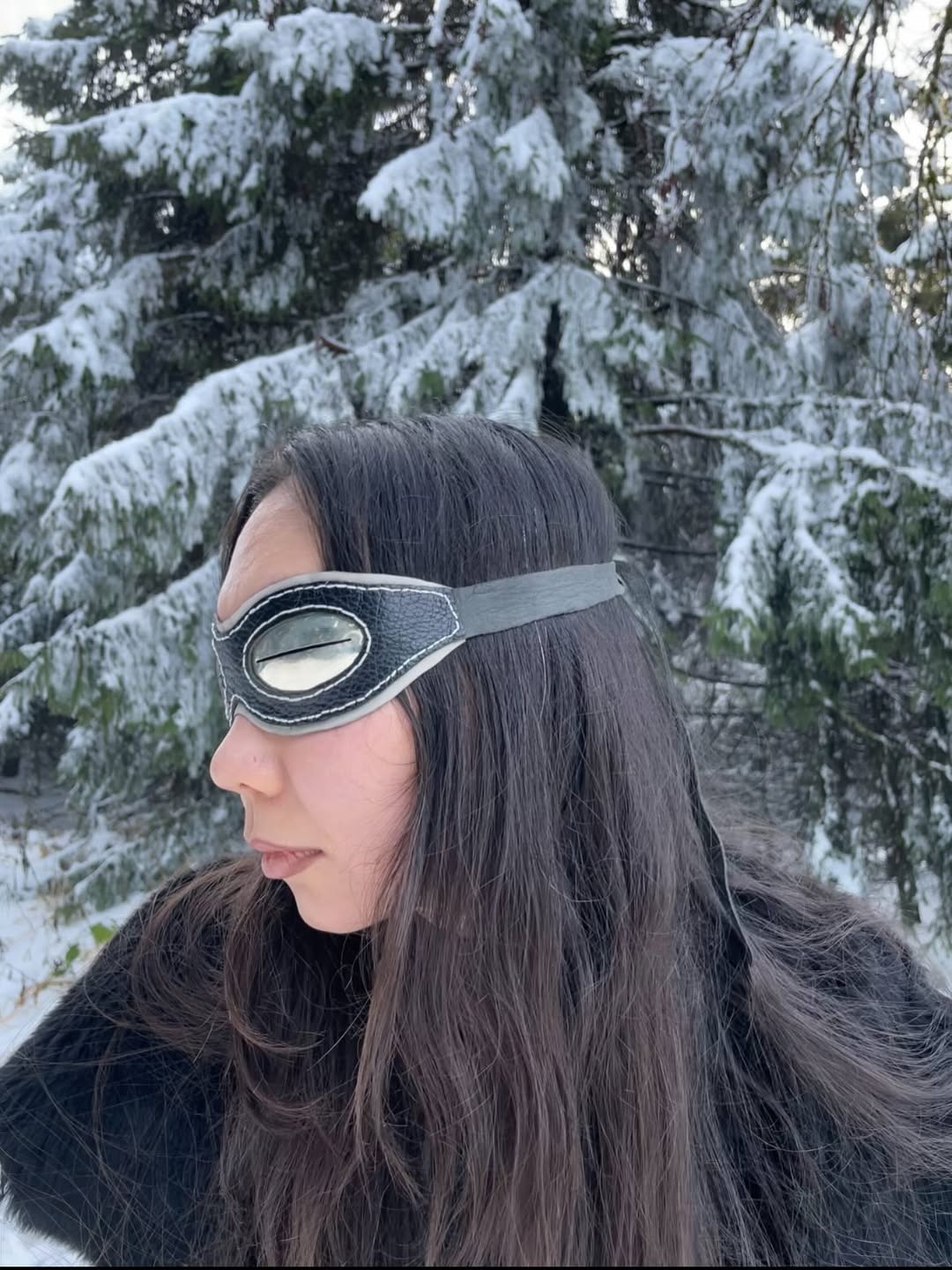 Silver snow goggles worn in profile against snowy spruce trees
